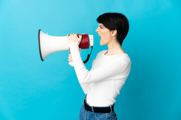 Woman with short hair isolated on blue background shouting through a megaphone to announce...