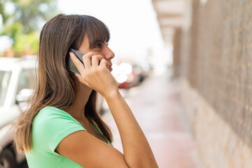 Young woman at outdoors keeping a conversation with the mobile phone with someone