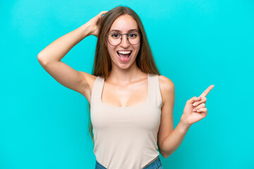 Young caucasian woman isolated on blue background surprised and pointing finger to the side