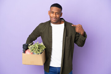 Latin man making a move while picking up a box full of things giving a thumbs up gesture