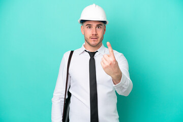 Young architect caucasian man with helmet and holding blueprints isolated on blue background doing coming gesture