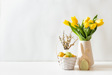 A white basket with eggs and a vase of yellow tulips on a white table