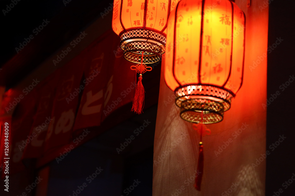 Poster a pair of red lanterns hang from the side of a building, illuminated by warm light.