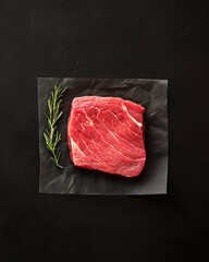 Piece of meat is on a black background with a piece of rosemary on top