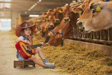 Charming child in a cowboy costume sings for cows on a farm in Denmark