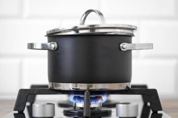 Blue flame from a domestic gas stove under a metal pot with a lid
