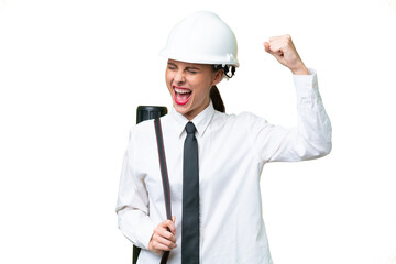 Young architect woman with helmet and holding blueprints over isolated background celebrating a victory