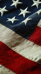 close-up of the American flag, showing detailed stitching, embroidered stars, and textured fabric. The red, white, and blue colors appear slightly aged, giving it a vintage and patriotic feel