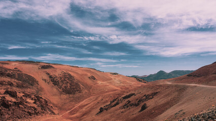 Scenic view to arid nature in caldera of Tenerife during summer hot day with hills, mountains, dunes and dark black volcanic rocks. Orange sand beautifully contrast with blue sky with clouds. Spain