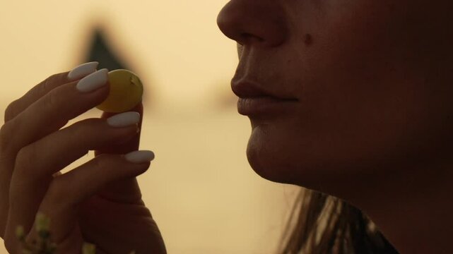 Woman Grape Food Closeup Portrait: A woman's hand holds a green grape close to her mouth, likely preparing to eat it. The photo is a closeup portrait.
