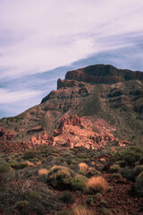 Steep cliff raises from the pampa red sand desert with rocky formations and tiny bushes in arid dry summer hot wasteland in caldera of Tenerife while hiking GR131. Canary Island.