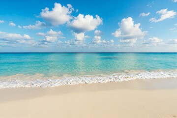 Fototapeta premium Serene beach scene with soft waves lapping against sandy shore under a bright blue sky dotted with fluffy white clouds.