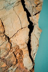 Fototapeta premium Close up view of a cracked, textured surface with a deep fissure, revealing earthy tones of tan, orange, and rust against a teal blue backdrop. The