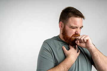 Young bearded man coughing over isolated blue background. Young man over grey wall is suffering...