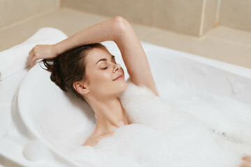 Serene young woman relaxing in a bubble bath, enjoying moments of tranquility and self-care at home, surrounded by soft foam and warm lighting.