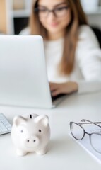 Young woman working on laptop at home with piggy bank in focus