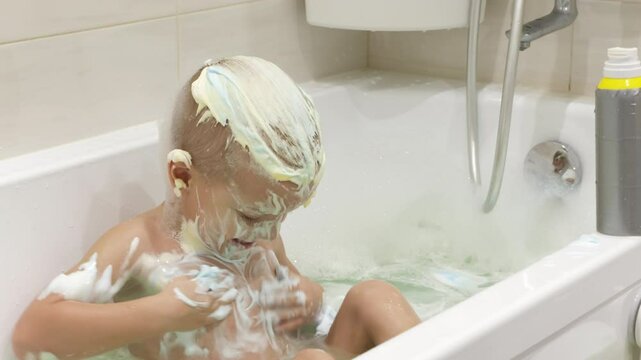 happy little boy is covered in bath foam. He is smiling and looking to the side while playing in the water.