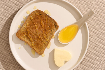 Close up view of delicious honey sandwich for breakfast. Creative modern composition with bread and butter toast with direct sunlight on beige background, top view    