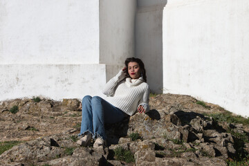 Fototapeta premium Latin brunette woman, young and beautiful is casually dressed and sitting on a big stone in the surroundings of cortegana castle in huelva, andalusia.