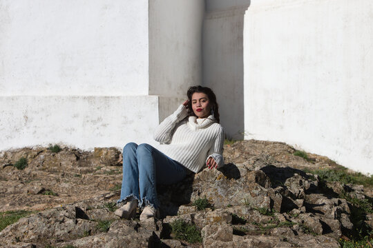 Latin brunette woman, young and beautiful is casually dressed and sitting on a big stone in the surroundings of cortegana castle in huelva, andalusia.