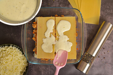 Top view. Homemade lasagna cooking preparation. Woman's hand use a spatula to spread the béchamel...