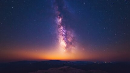 Fototapeta premium Milky way rising over distant town lights and mountain range at sunset