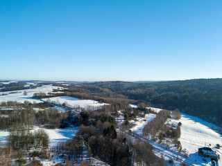 Aerial view of snow-covered fields and trees under a clear blue sky, showcasing a serene winter landscape. Perfect for nature-related projects.