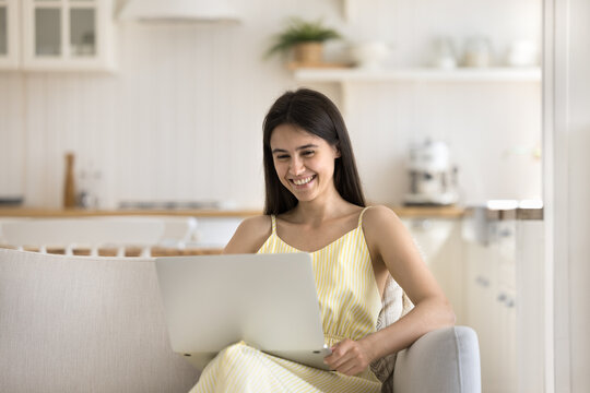 Free summer day online. Happy smiling young woman spend leisure time at home on comfy sofa relax playing computer game on notebook laugh speaking on video call in app watch funny video at social media