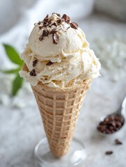 Un helado cremoso de vainilla en un cono, decorado con chispas de chocolate, sobre un fondo claro y suave.