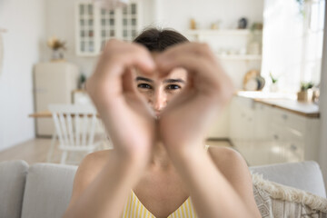 I love you. Affectionate portrait happy teen girl sit on sofa look at camera through heart formed...