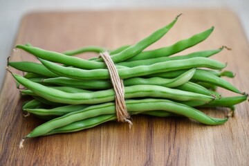 Fototapeta premium Fresh green beans are bundled and tied with rustic twine, showcasing vibrant color and texture against a wooden background, highlighting the freshness and quality of the produce