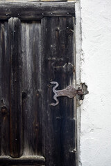 Antique metal ornate forged door hinge holding a weathered wooden door that has darkened with age. Copy space for text.