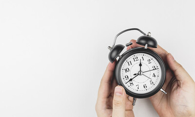 Hand holding a black alarm clock on white background, with copy space. Concepts of time management, appointment hours, and overtime.
