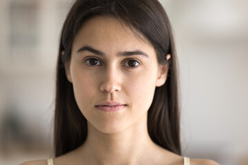 Naklejka premium Cropped close up portrait calm face of beautiful female teenager with brown eyes long dark hair smooth healthy skin looking at camera. Skincare self care natural beauty of youth or confidence concept