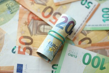 Roll of twenty euro currency bills lies on big amount of hundred and fifty euro banknotes