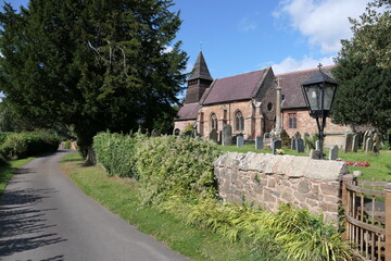 A quaint old English church stands peacefully along a quiet country lane, its weathered stone walls and ivy-clad tower blending into the rural landscape. 