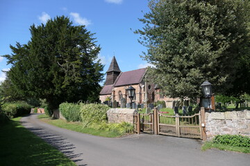 A quaint old English church stands peacefully along a quiet country lane, its weathered stone walls and ivy-clad tower blending into the rural landscape. 