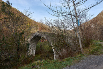 Historic medieval bridge over the Dobra river surrounded by lush nature in Asturias, Spain