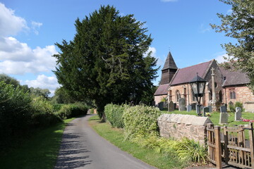 A quaint old English church stands peacefully along a quiet country lane, its weathered stone walls and ivy-clad tower blending into the rural landscape. 