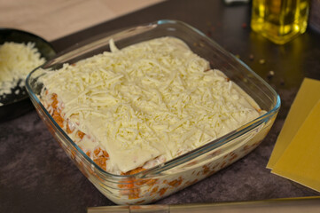 Homemade lasagna cooking preparation. Grated cheese, Bolognese sauce in a glass form. Lasagna pasta sheets. Cheese in a black bowl. Black background