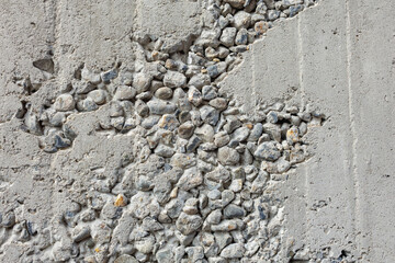 Rough concrete wall displays exposed aggregate, revealing a rugged surface of mixed stones. The...