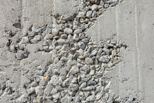Rough concrete wall displays exposed aggregate, revealing a rugged surface of mixed stones. The contrasting textures highlight the raw, natural elements embedded within the structure.