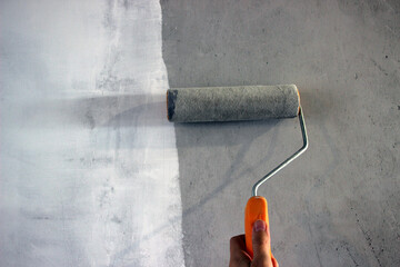 Worker is using a paint roller to apply a white substance, likely adhesive or primer, onto a...