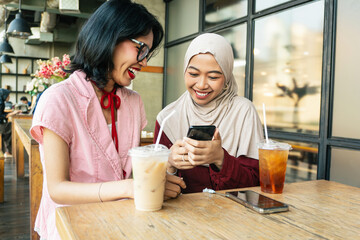 Two asian female friends having fun in the weekend using cell phone app to share content on social...