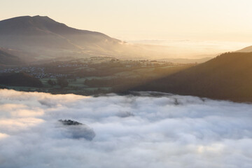Obraz premium Golden spring sunlight on Blencathra mountain overlooking calm misty Derwentwater, Lake District, UK.