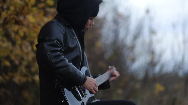 man plays electric guitar gloomily outdoors in cloudy weather