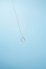 Minimalist silver necklace with a ring pendant suspended against a calming blue background. Jewelry style.