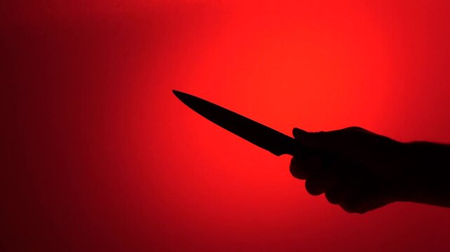 Silhouette of hand holding knife on red background