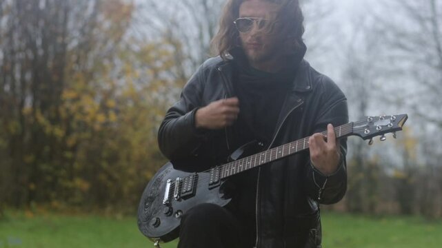 man plays electric guitar gloomily outdoors in cloudy weather