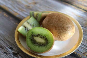 A whole kiwi and a sliced kiwi on a plate on a rustic table. Freshly sliced kiwi fruit. 